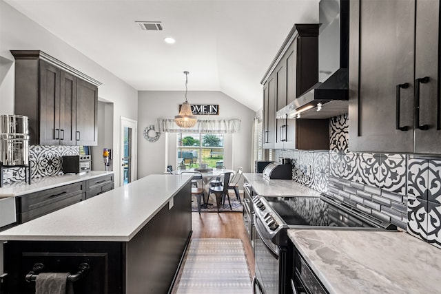 kitchen with tasteful backsplash, wall chimney exhaust hood, vaulted ceiling, decorative light fixtures, and stainless steel electric range oven