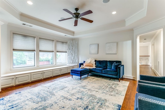 living room with hardwood / wood-style floors, ornamental molding, and a raised ceiling