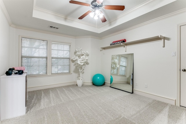 workout area featuring ceiling fan, light colored carpet, ornamental molding, and a raised ceiling