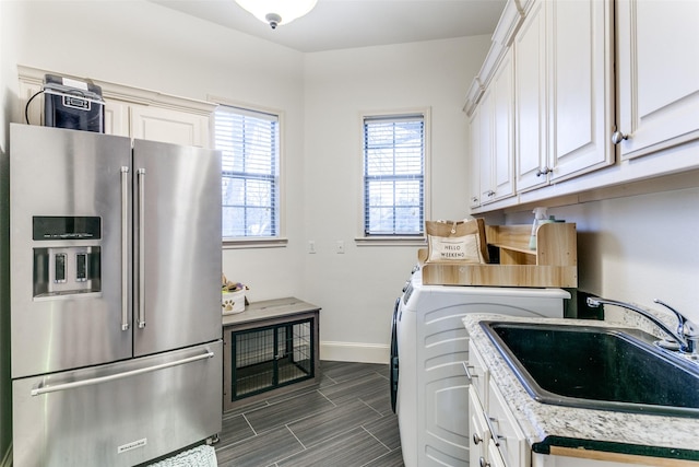 kitchen with washer / clothes dryer, white cabinetry, sink, and high end refrigerator