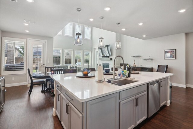 kitchen featuring gray cabinetry, a kitchen island with sink, stainless steel dishwasher, hanging light fixtures, and sink