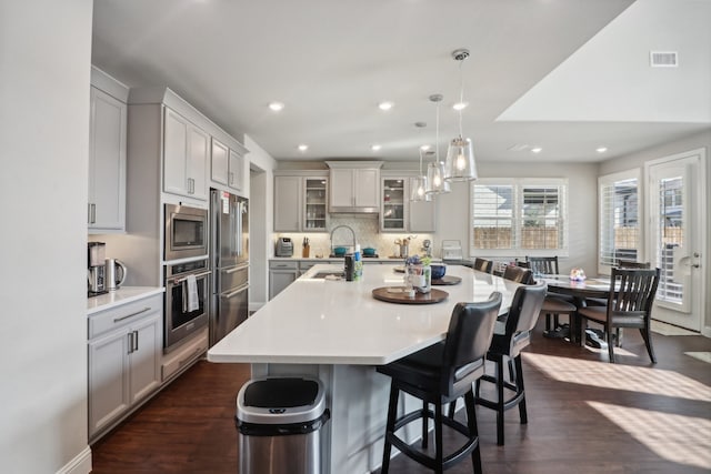 kitchen with decorative light fixtures, stainless steel appliances, a large island, dark hardwood / wood-style floors, and a breakfast bar area