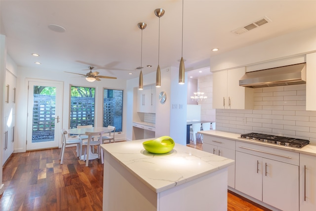 kitchen featuring a center island, wall chimney range hood, hanging light fixtures, white cabinetry, and stainless steel gas cooktop