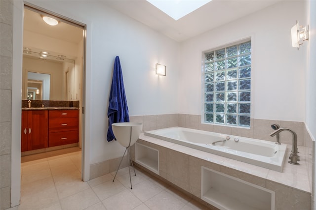 bathroom featuring tile patterned flooring, vanity, a relaxing tiled tub, and a skylight