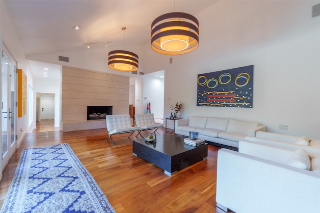 living room featuring hardwood / wood-style floors, high vaulted ceiling, and a tiled fireplace