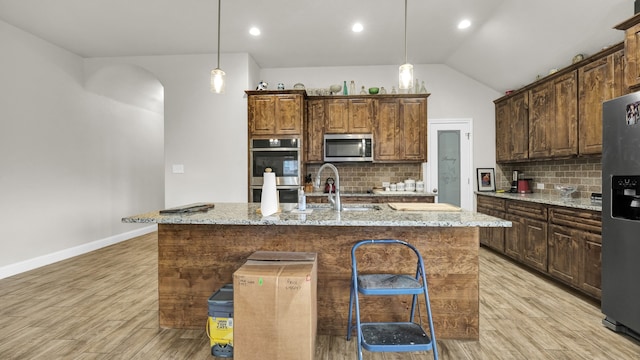 kitchen with a center island with sink, light hardwood / wood-style flooring, light stone counters, and appliances with stainless steel finishes