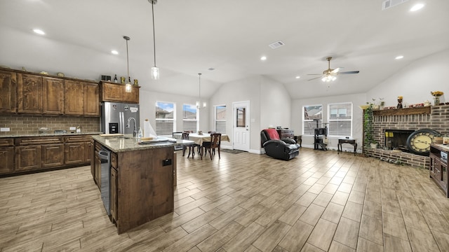 kitchen featuring lofted ceiling, a brick fireplace, an island with sink, and ceiling fan