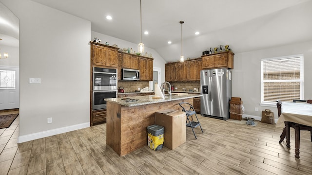 kitchen featuring light hardwood / wood-style flooring, appliances with stainless steel finishes, light stone counters, a kitchen bar, and a center island with sink