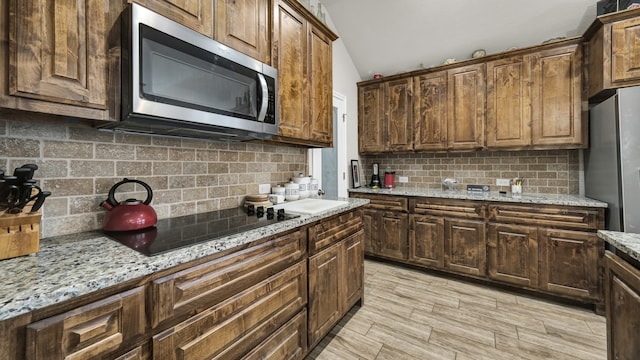 kitchen with appliances with stainless steel finishes, vaulted ceiling, light stone countertops, and decorative backsplash