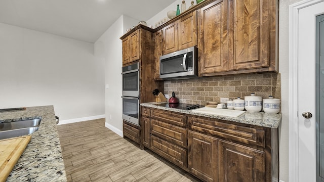 kitchen with decorative backsplash, appliances with stainless steel finishes, light stone countertops, and light hardwood / wood-style floors