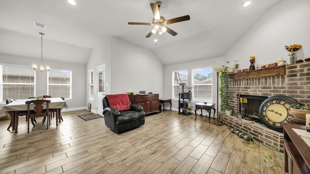 living room featuring lofted ceiling, ceiling fan with notable chandelier, light hardwood / wood-style floors, and a brick fireplace