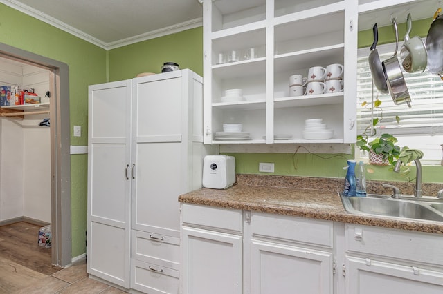 kitchen with white cabinets, light wood-type flooring, light stone countertops, sink, and ornamental molding