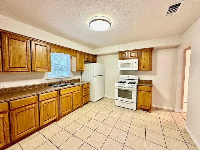 kitchen with a textured ceiling, sink, light tile patterned floors, and white appliances