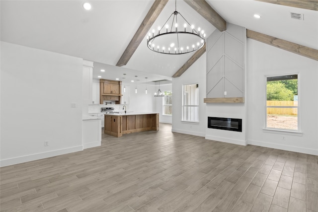 unfurnished living room with a wealth of natural light, a fireplace, beam ceiling, and a notable chandelier