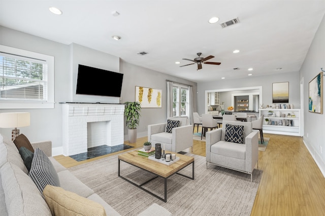 living room featuring a brick fireplace, light hardwood / wood-style flooring, and ceiling fan