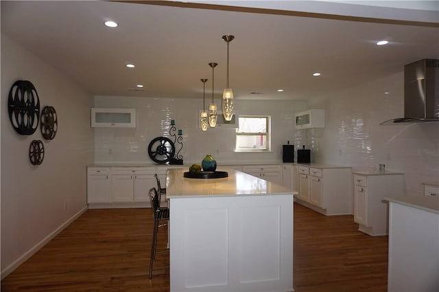 kitchen with wall chimney exhaust hood, dark hardwood / wood-style flooring, a kitchen island, and white cabinets