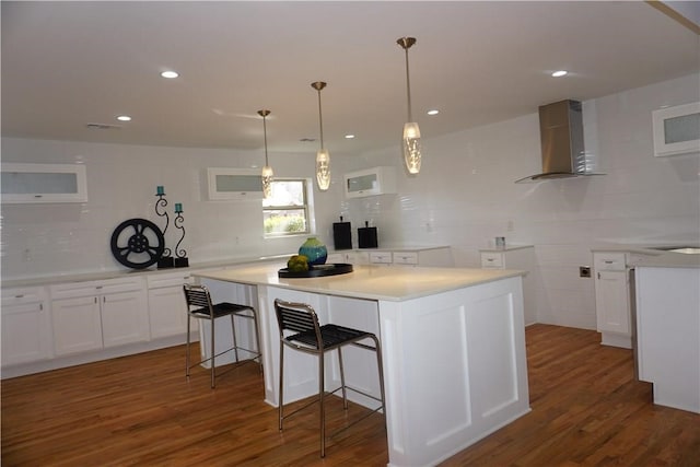 kitchen with backsplash, hardwood / wood-style floors, white cabinetry, wall chimney range hood, and a kitchen island