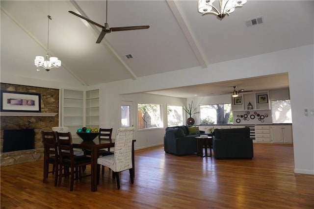 dining room featuring high vaulted ceiling, built in shelves, ceiling fan with notable chandelier, dark hardwood / wood-style floors, and a stone fireplace