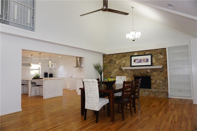 dining room with a high ceiling, ceiling fan with notable chandelier, hardwood / wood-style floors, and a fireplace