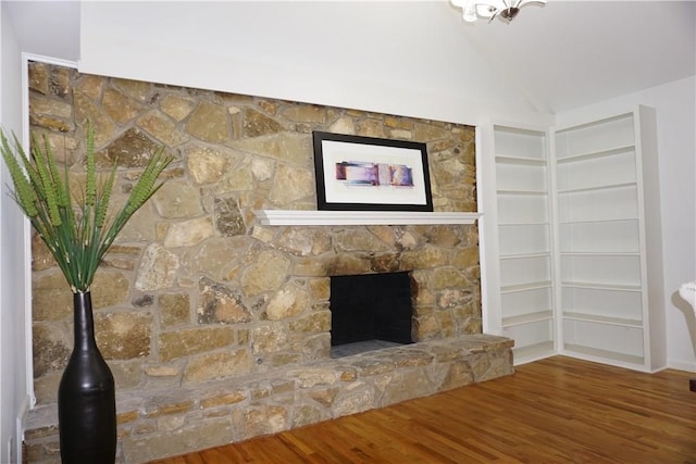 room details with built in shelves, hardwood / wood-style floors, and a stone fireplace