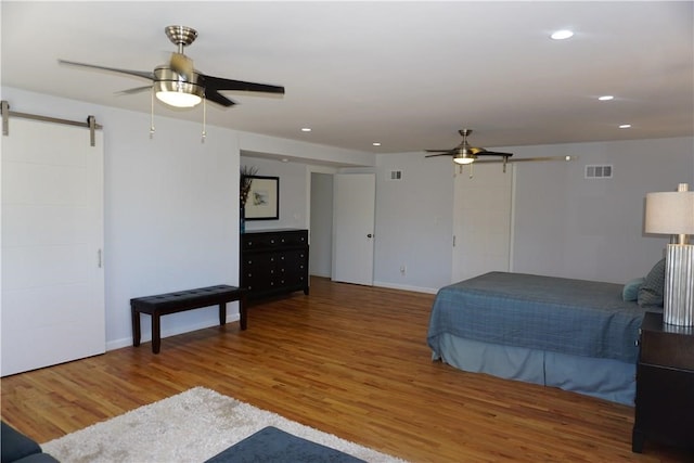 bedroom featuring hardwood / wood-style floors, ceiling fan, and a barn door