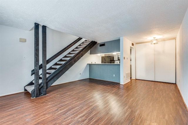 unfurnished living room featuring a textured ceiling, wood finished floors, visible vents, baseboards, and stairway