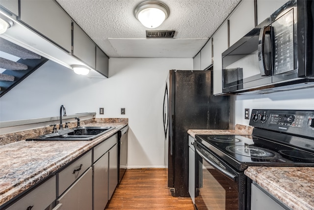 kitchen featuring hardwood / wood-style floors, sink, gray cabinets, black appliances, and a textured ceiling