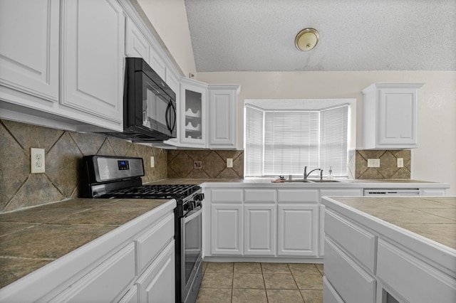 kitchen with light tile patterned floors, tile counters, gas stove, lofted ceiling, and white cabinets