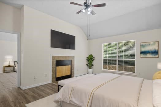 bedroom with ceiling fan, vaulted ceiling, hardwood / wood-style flooring, and a fireplace