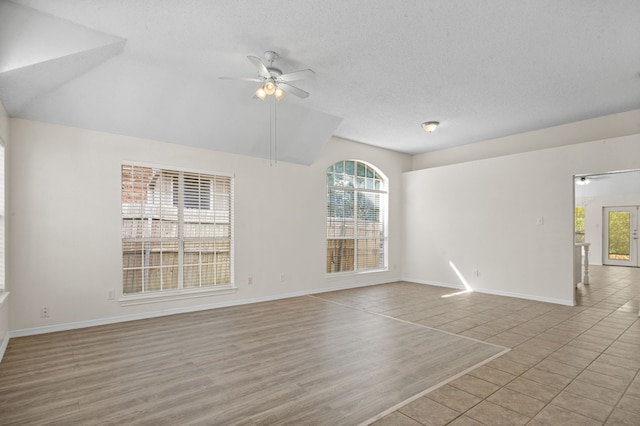 empty room featuring a textured ceiling, light hardwood / wood-style flooring, ceiling fan, and vaulted ceiling