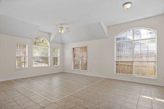 tiled spare room with lofted ceiling, ceiling fan, and a textured ceiling