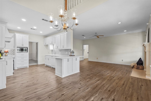 kitchen featuring backsplash, ceiling fan with notable chandelier, light hardwood / wood-style flooring, white cabinets, and hanging light fixtures