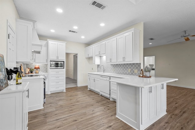 kitchen featuring white dishwasher, light hardwood / wood-style floors, white cabinets, and kitchen peninsula