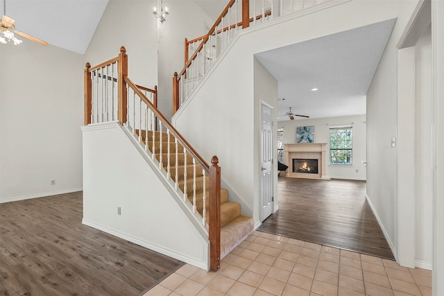 stairs with wood-type flooring, high vaulted ceiling, and ceiling fan