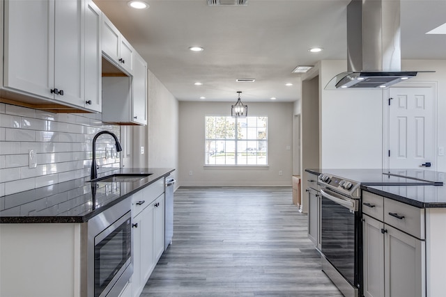 kitchen with light wood-type flooring, backsplash, stainless steel appliances, island range hood, and sink