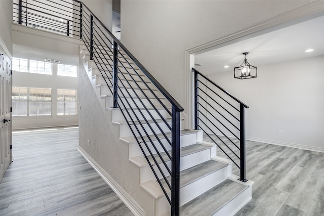 staircase with wood-type flooring and an inviting chandelier