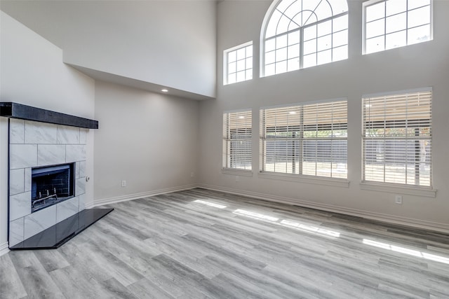 unfurnished living room with a high ceiling, a fireplace, plenty of natural light, and light hardwood / wood-style flooring