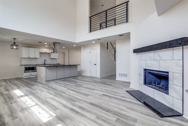 unfurnished living room with a towering ceiling, a tile fireplace, sink, and light hardwood / wood-style flooring