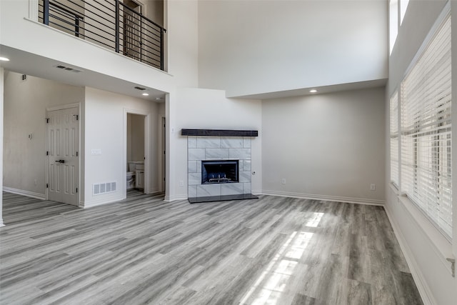 unfurnished living room featuring a towering ceiling, light hardwood / wood-style flooring, and a tile fireplace