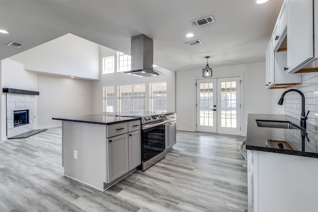 kitchen featuring a fireplace, light hardwood / wood-style flooring, stainless steel electric range, island range hood, and sink