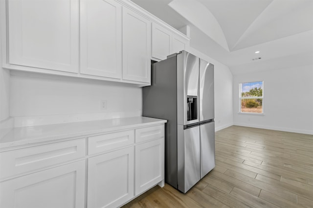 kitchen featuring light wood-type flooring, white cabinets, stainless steel fridge with ice dispenser, and vaulted ceiling