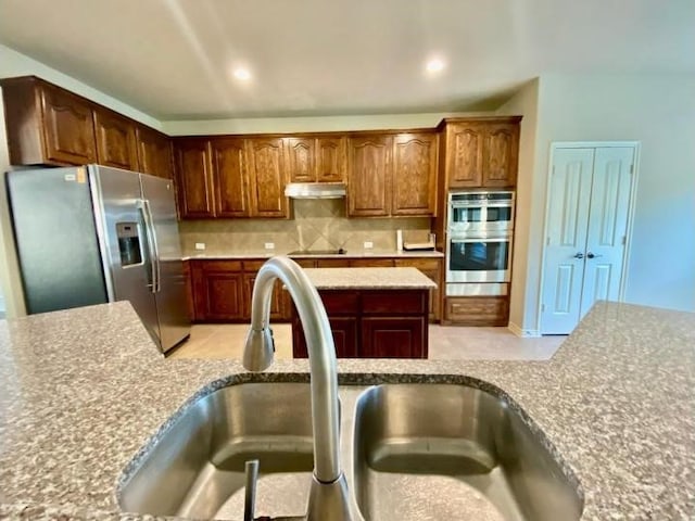 kitchen with backsplash, stainless steel appliances, light stone countertops, and sink