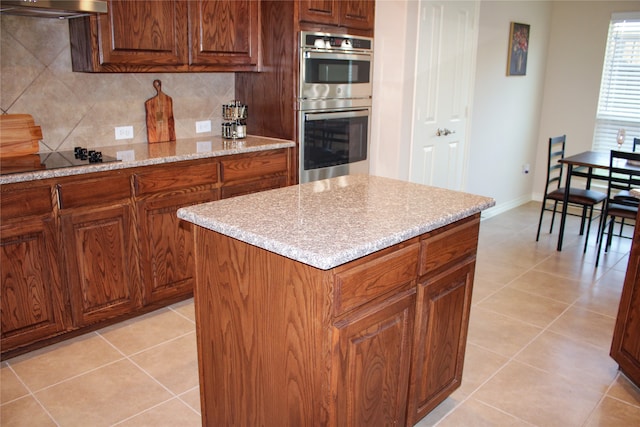 kitchen with tasteful backsplash, light tile patterned floors, a kitchen island, range hood, and stainless steel double oven