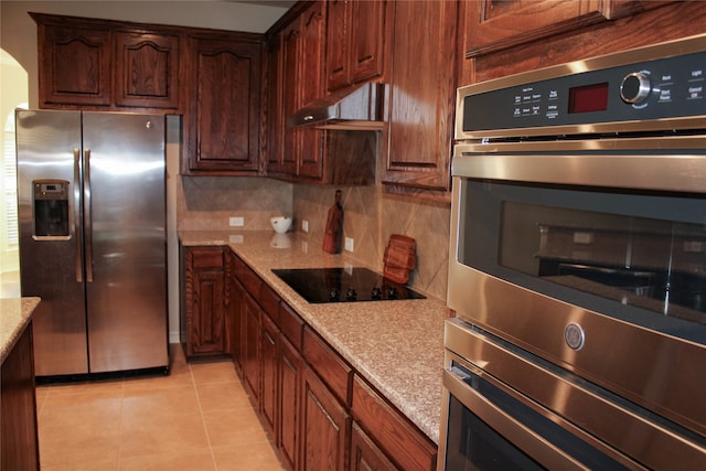 kitchen featuring decorative backsplash, range hood, light tile patterned floors, appliances with stainless steel finishes, and light stone counters