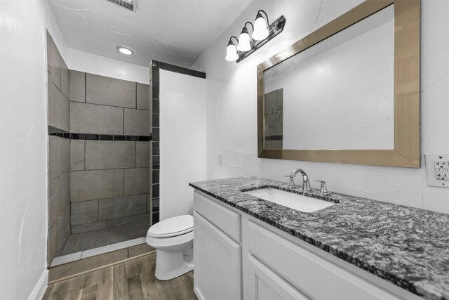 bathroom with a tile shower, hardwood / wood-style floors, vanity, and toilet