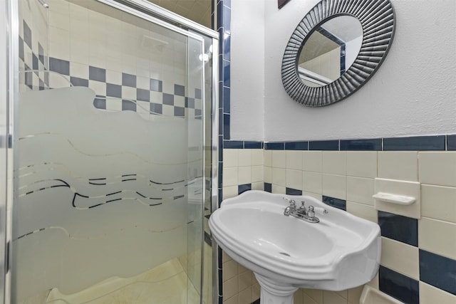 bathroom featuring a shower with door, sink, and tile walls