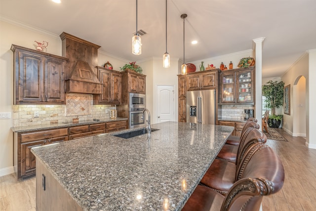 kitchen with appliances with stainless steel finishes, sink, dark stone countertops, a large island, and light wood-type flooring