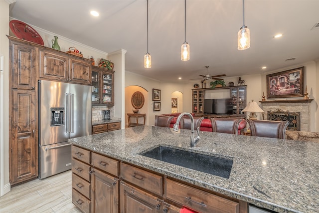 kitchen featuring high end fridge, decorative light fixtures, sink, ceiling fan, and a stone fireplace