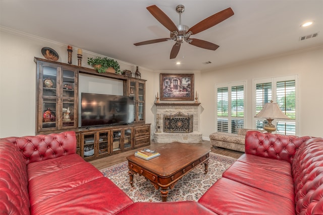 living room featuring ornamental molding, wood-type flooring, ceiling fan, and a stone fireplace