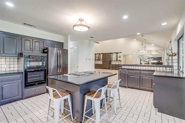 kitchen featuring gray cabinets, backsplash, a kitchen breakfast bar, a center island, and appliances with stainless steel finishes